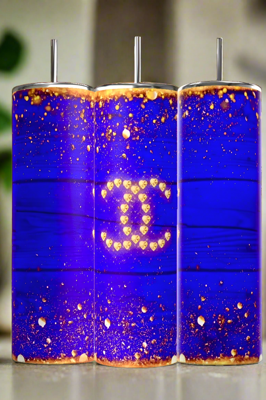 The Kreative Kreationz Chanel 20oz Skinny Tumbler in royal blue features a bold blue and gold glitter design with a gold Chanel logo, complemented by metal straws—luxurious, elegant drinkware perfect for any occasion.