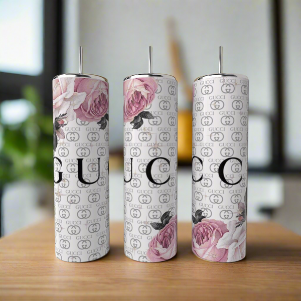 Three tall Kreative Kreationz Gucci Inspired 20oz Tumblers, featuring pink rose designs and repeating logo patterns, are displayed on a wooden surface in a blurred indoor setting, highlighting stylish luxury drinkware.