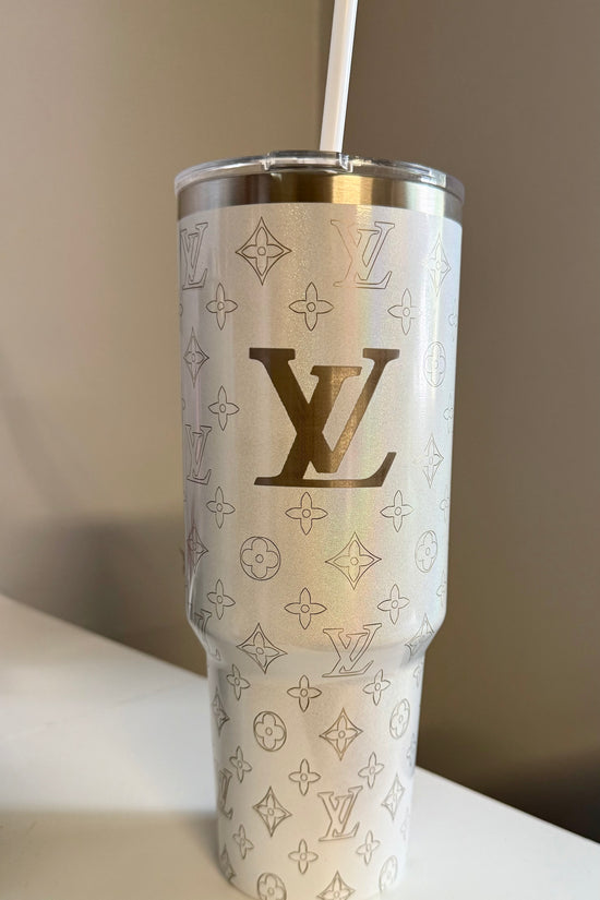 The LV White 40oz Engraved Tumbler by Kreative Kreationz, featuring a gold Louis Vuitton monogram and pattern, with a stainless steel straw, sits on a white surface against a neutral background.