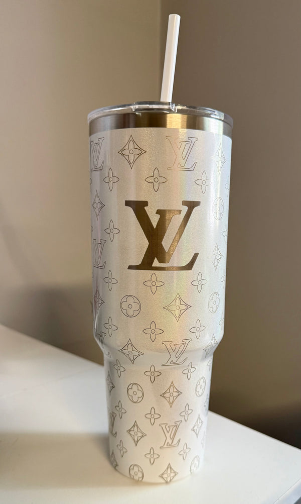 The LV White 40oz Engraved Tumbler by Kreative Kreationz, featuring a gold Louis Vuitton monogram and pattern, with a stainless steel straw, sits on a white surface against a neutral background.