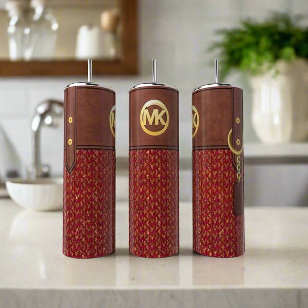 Three MK 20oz Tumblers in brown and red by Kreative Kreationz with gold logos and metallic spouts are on a kitchen counter, resembling Michael Kors products. A faucet, shelf, and green plant appear blurred in the background.