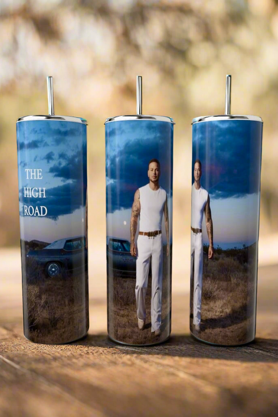 Three Kane Brown The High Road 20oz Tumblers by Kreative Kreationz are displayed outdoors, featuring lids and straws. They depict a man in a white outfit, a classic car, and 