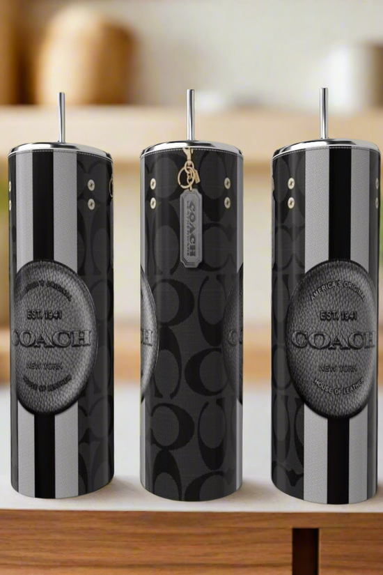 Three tall, stylish tumblers with straws sit on a counter, showcasing sleek luxury-inspired designs with bold monochrome patterns. Each features the brand name 