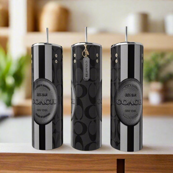 Three tall, stylish tumblers with straws sit on a counter, showcasing sleek luxury-inspired designs with bold monochrome patterns. Each features the brand name "Kreative Kreationz." The softly blurred kitchen background enhances the elegance of these Coach 20oz Tumblers.