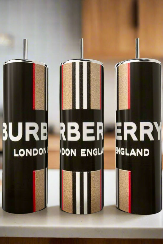 Three Burberry 20oz Skinny Tumblers by Kreative Kreationz, featuring bold black, white, and red designs on stainless steel luxury drinkware with straws, stand on a kitchen counter against a blurred background.