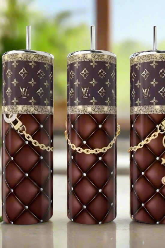Three LV Handbag Inspired 20oz Tumblers by Kreative Kreationz, featuring quilted brown and gold chain designs with patterned tops, are elegantly displayed on a kitchen counter with mint leaves nearby.
