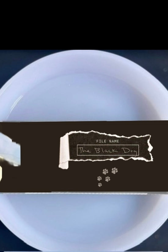A white mug with a light blue handle is shown against a plain background. On top of the Kreative Kreationz Black Dog lid Plate/Topper, which fits 20, 30, and 40 oz Stanley cups, is a partially unwrapped chocolate bar with a black wrapper.