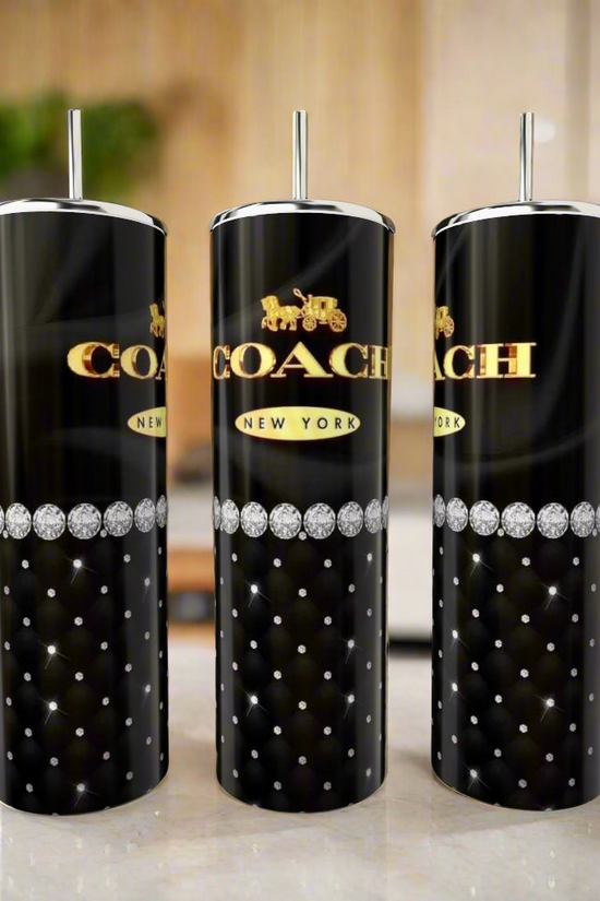 Three Coach Pearl Black & Gold 20oz Skinny Tumblers by Kreative Kreationz, featuring quilted diamond patterns, silver straws, and a gold logo, are displayed on a kitchen counter with a blurred background.