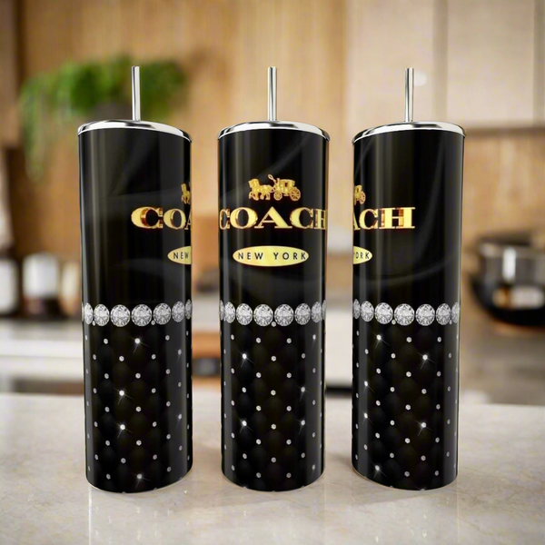 Three Coach Pearl Black & Gold 20oz Skinny Tumblers by Kreative Kreationz, featuring quilted diamond patterns, silver straws, and a gold logo, are displayed on a kitchen counter with a blurred background.