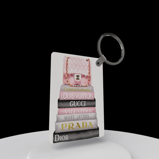 The Designer Inspired Keychain by Kreative Kreationz features a pink quilted purse atop stacked luxury brand books against a black background—a stylish accessory and perfect gift for fashion lovers!.