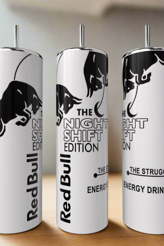 Three tall, white Red Bull Night Shift Edition 20oz Tumblers by Kreative Kreationz stand on a wooden surface, featuring a luxury-inspired design with a black bull and bold black text. A blurred plant appears in the background.