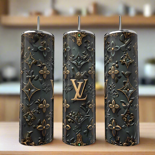 The LV 20oz Tumbler by Kreative Kreationz features a tall, cylindrical stainless steel design with straws and an embossed gold and black pattern, adding a touch of luxury to your drinkware collection. Displayed on wood with a blurred kitchen background.
