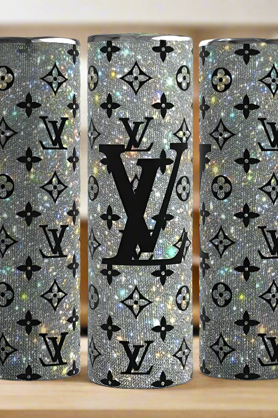 Three Kreative Kreationz Louis Vuitton Shimmer 20oz Tumblers with silver glitter finish, black LV-inspired logos, and monogram patterns are displayed on a wooden surface against a blurred kitchen background.