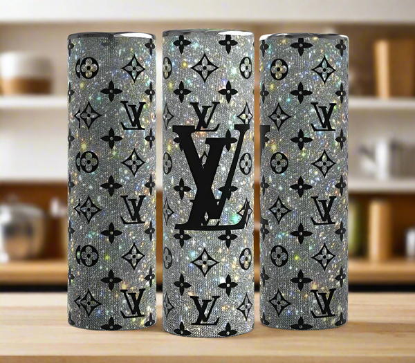 Three Kreative Kreationz Louis Vuitton Shimmer 20oz Tumblers with silver glitter finish, black LV-inspired logos, and monogram patterns are displayed on a wooden surface against a blurred kitchen background.