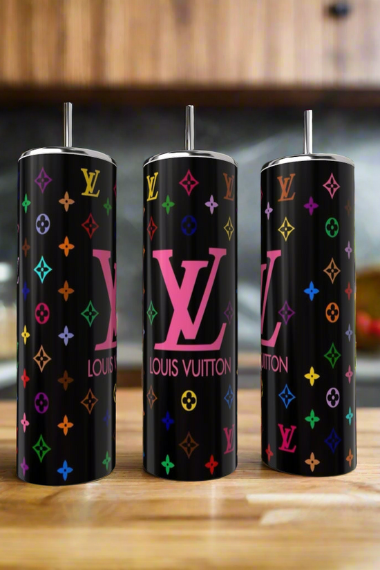 The Kreative Kreationz Louis V 20oz Skinny Tumbler set includes three luxury-inspired tumblers with metal straws, black backgrounds, and colorful designs, shown on a wooden kitchen counter with a blurred kitchen backdrop.