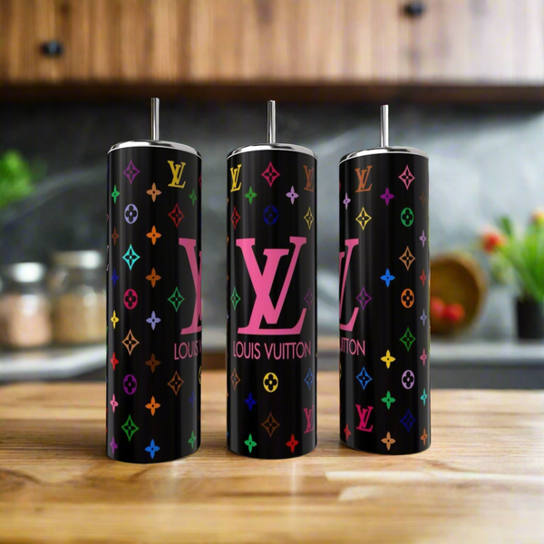 The Kreative Kreationz Louis V 20oz Skinny Tumbler set includes three luxury-inspired tumblers with metal straws, black backgrounds, and colorful designs, shown on a wooden kitchen counter with a blurred kitchen backdrop.