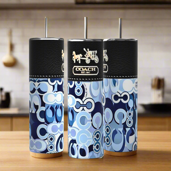 Three tall Coach Purse 20oz Tumblers by Kreative Kreationz, featuring black lids, are arranged on a wooden surface in a modern kitchen—stylish reusable drinkware perfect for any setting.