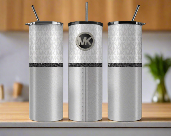 Three MK Grey Designer Inspired 20oz Tumblers by Kreative Kreationz sit on the counter, each with silver straws, a subtle "MK" pattern, black glittery stripe, and an elegant round "MK" logo on the front.