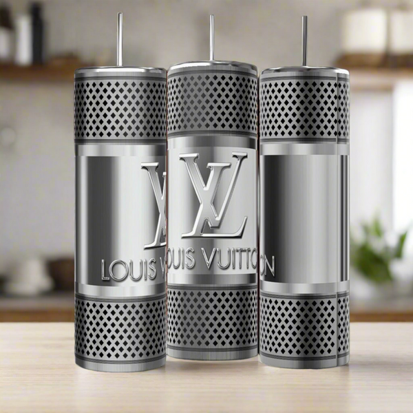 Three LV Silver Stainless Steel 20oz Tumblers by Kreative Kreationz stand upright on a wooden surface, showcasing luxury-inspired design, engraved branding and logo, perforations, and metal straws against a blurred kitchen background.