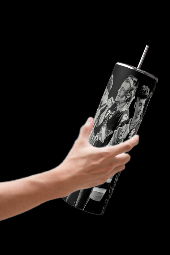 A hand is holding the Kreative Kreationz One Direction B&W 20oz Stainless Steel Tumbler against a black background. This sleek tumbler showcases monochrome images of various animated characters with playful expressions and is equipped with a spill-proof lid for convenience.