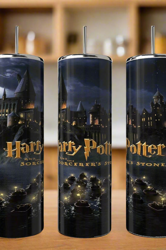 The Kreative Kreationz Harry Potter 20oz tall, cylindrical tumblers feature a Sorcerer's Stone design showing Hogwarts at night with boats on a lake and the title. These skinny tumblers are perfect for use with a reusable straw and are set on a wooden countertop.