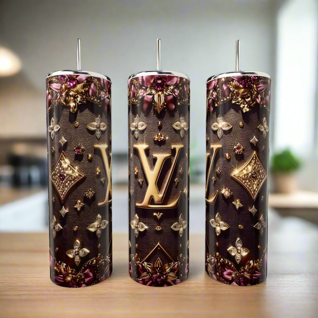 Three 20oz LV Purple & Gold tumblers by Kreative Kreationz, featuring luxury-inspired stainless steel with ornate gold and purple designs, are showcased on a wooden countertop in a softly lit room.