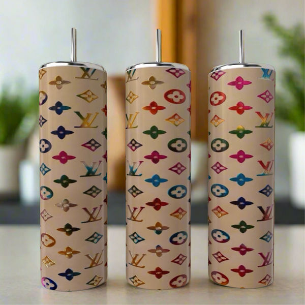 Three tall Louis Vuitton Purse Designed 20oz Tumblers by Kreative Kreationz, each with a metal straw, feature colorful LV-inspired patterns and logos. The softly blurred background has green plants and neutral tones for elegance.