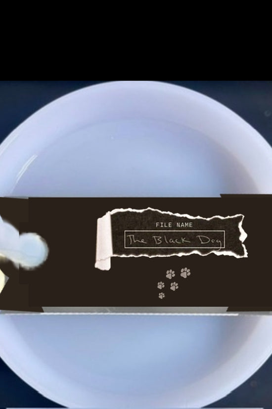 A white mug with a light blue handle is shown against a plain background. On top of the Kreative Kreationz Black Dog lid Plate/Topper, which fits 20, 30, and 40 oz Stanley cups, is a partially unwrapped chocolate bar with a black wrapper.