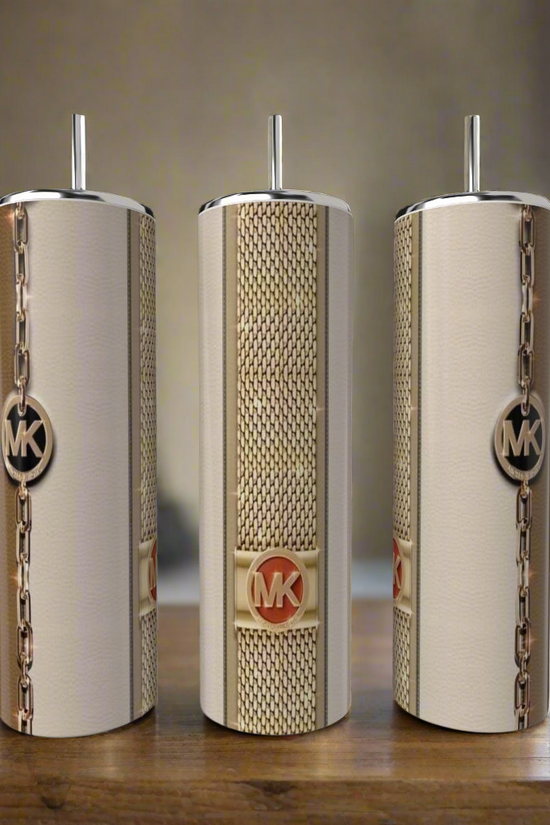 Three stylish Kreative Kreationz Pink MK 20oz Tumblers with metal straws sit on a wooden surface. Each stainless steel piece features a gold MK logo and chain-link design, set against a blurred kitchen backdrop.