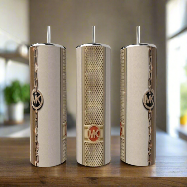 Three stylish Kreative Kreationz Pink MK 20oz Tumblers with metal straws sit on a wooden surface. Each stainless steel piece features a gold MK logo and chain-link design, set against a blurred kitchen backdrop.