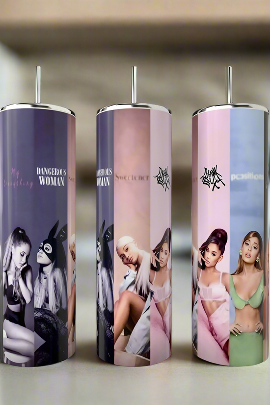 Three Kreative Kreationz Ariana Grande All Albums 20oz Tumblers, featuring images of Ariana in various poses and outfits, are placed on a table against a blurred indoor background.