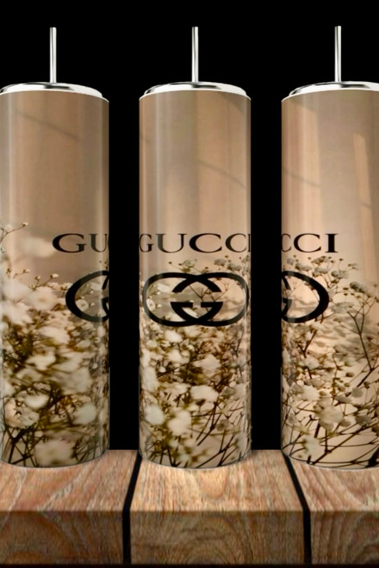 Three tall GUCCI Gold Collection 20oz Skinny Tumblers by Kreative Kreationz, each with metal straws, feature a beige background, white floral pattern, and black Gucci logo. They are displayed on wood against a dark backdrop.