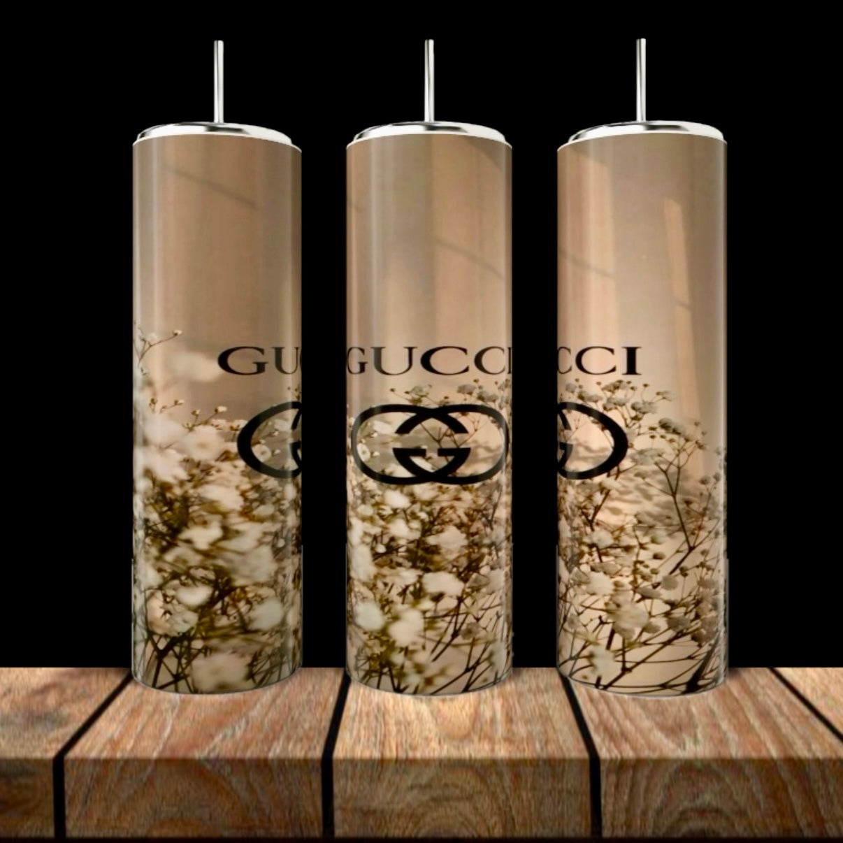 Three tall GUCCI Gold Collection 20oz Skinny Tumblers by Kreative Kreationz, each with metal straws, feature a beige background, white floral pattern, and black Gucci logo. They are displayed on wood against a dark backdrop.