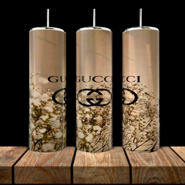 Three tall GUCCI Gold Collection 20oz Skinny Tumblers by Kreative Kreationz, each with metal straws, feature a beige background, white floral pattern, and black Gucci logo. They are displayed on wood against a dark backdrop.