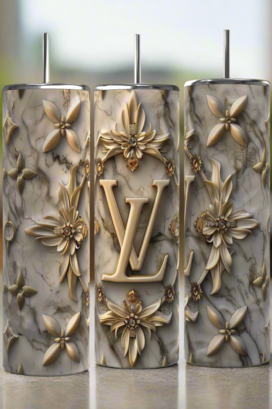 The Kreative Kreationz Louis Vuitton Silver Gold 20oz Tumblers feature gold floral designs, a bold LV monogram, metallic straws, and marble-patterned stainless steel, presenting a luxury-inspired look against a softly blurred background.