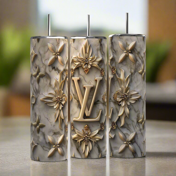 The Kreative Kreationz Louis Vuitton Silver Gold 20oz Tumblers feature gold floral designs, a bold LV monogram, metallic straws, and marble-patterned stainless steel, presenting a luxury-inspired look against a softly blurred background.