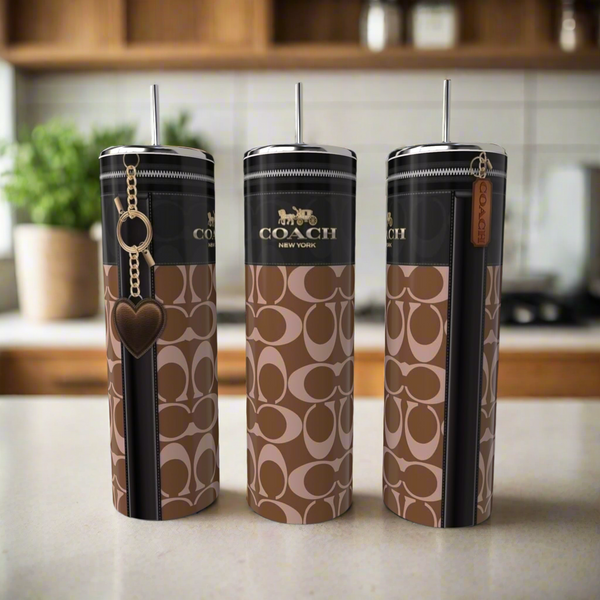 Three stylish, eco-friendly C Buckle 20oz Skinny Tumblers by Kreative Kreationz, featuring a brown and black pattern and made of high-quality stainless steel, grace the kitchen counter. Each tumbler sports a unique charm: a heart, zipper pull, and leather tag—a perfect blend of luxury-inspired design.