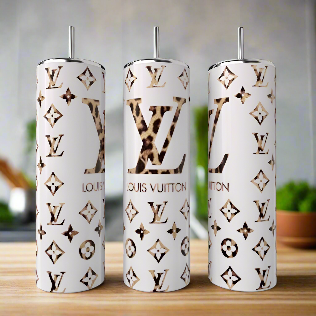 Three Kreative Kreationz LV Designed 20oz Tumblers with metal straws feature gold and leopard print accents, Louis Vuitton-inspired monogram, and high-quality stainless steel, shown on a wooden surface in a modern kitchen.