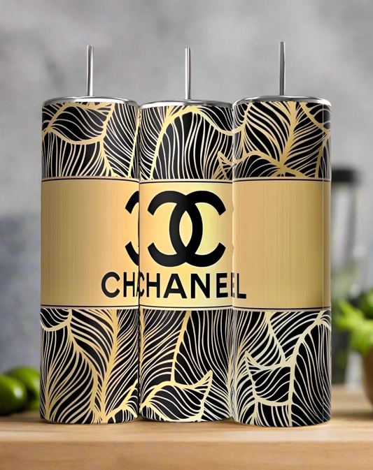Three Chanel 20oz Skinny Tumblers by Kreative Kreationz, featuring black and gold leaf patterns with a central gold band displaying the Chanel logo and "CHANEL," are shown on a wooden surface.