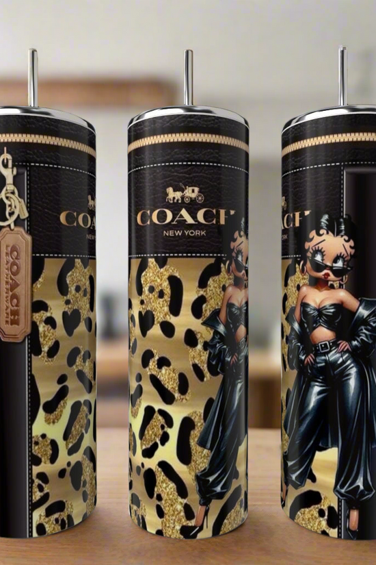 Three Kreative Kreationz 20oz tumblers, including the Betty Boop Gold, are shown from different angles on a wooden surface with gold and black leopard print and unique designs.