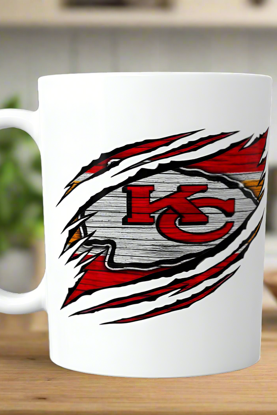 The Chiefs Ceramic Mug | 11oz by Kreative Kreationz features a sublimated design that appears to tear through the white ceramic, showcasing the bold red, yellow, and white Kansas City Chiefs logo—perfect for any cozy kitchen.