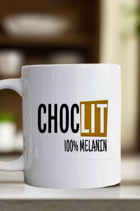 The Choc-Lit Mug by Kreative Kreationz sits on a kitchen counter, displaying “CHOC LIT 100% MELANIN” in bold black and gold letters, with shelves and plants softly blurred in the background.