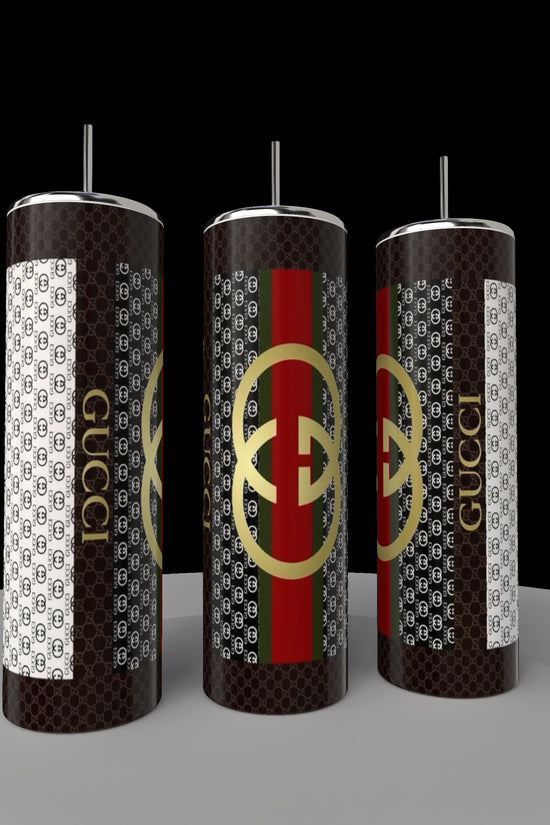 Three Gucci 20oz Tumblers by Kreative Kreationz sit on a round platform, featuring a black, white, red, and green pattern with overlapping letters. Made from high-quality stainless steel, these eco-friendly tumblers include straws and showcase a luxury-inspired design.