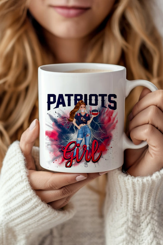 A woman in a white sweater holds the Patriots Girl Ceramic Mug | 11oz by Kreative Kreationz, featuring a sublimated design of a woman in jeans and a Patriots shirt on a red, white, and blue splatter background.