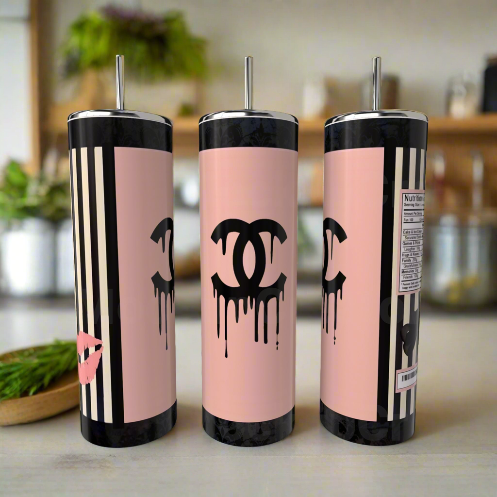 Three Kreative Kreationz Chanel 20oz Skinny Tumblers, pink with black dripping logos, stripes, and metal straws rest on a counter; one shows a kiss mark and another a playful nutrition label for eco-friendly drinkware style.