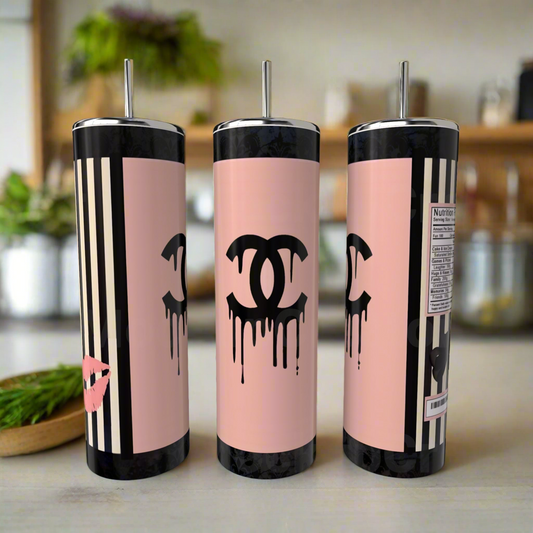 Three Kreative Kreationz Chanel 20oz Skinny Tumblers, pink with black dripping logos, stripes, and metal straws rest on a counter; one shows a kiss mark and another a playful nutrition label for eco-friendly drinkware style.