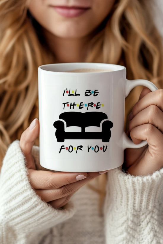 A woman with long, wavy hair holds a Kreative Kreationz Friends Couch Mug, a white ceramic piece decorated with 