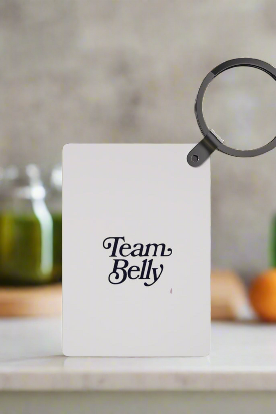 A Team Belle Inspired Keychain from Kreative Kreationz is displayed upright on a kitchen counter, making a perfect gift. Jars and vegetables are blurred in the background for a cozy touch.