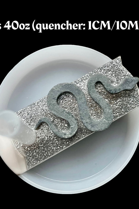 A close-up image shows a plastic straw with a silver glittery cover and snake-shaped decoration on a white Stanley tumbler lid topper. The text above the lid reads, 