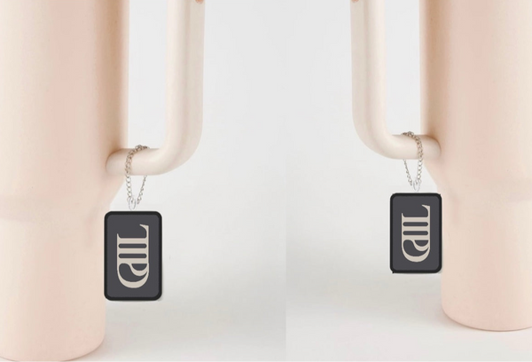 Two identical light pink vases with wide handles feature distinctive designs. Each handle has a TTPD Charm Dangle by Kreative Kreationz, displaying a black tumbler charm with vertical script resembling "MILL." The vases are set against a neutral backdrop.